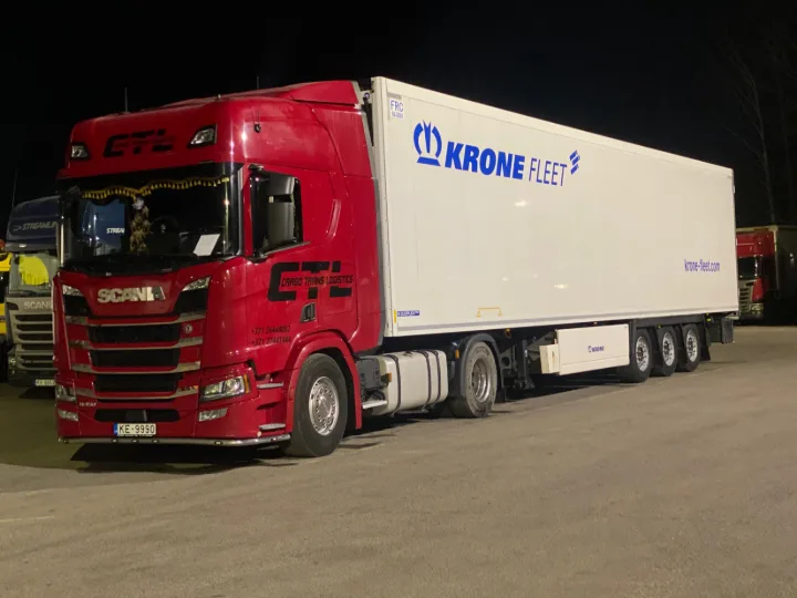 A red Scania with a Krone reefer trailer, loaded at night